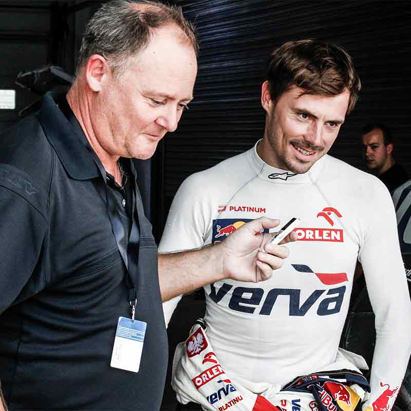 Neil Perkins holds a microphone up to Rally Driver, Jakub Kuba Przygonski as he interviews him.