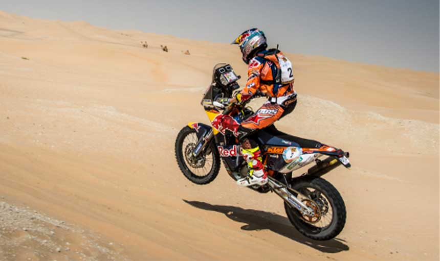 A man on a motorbike races through the desert.