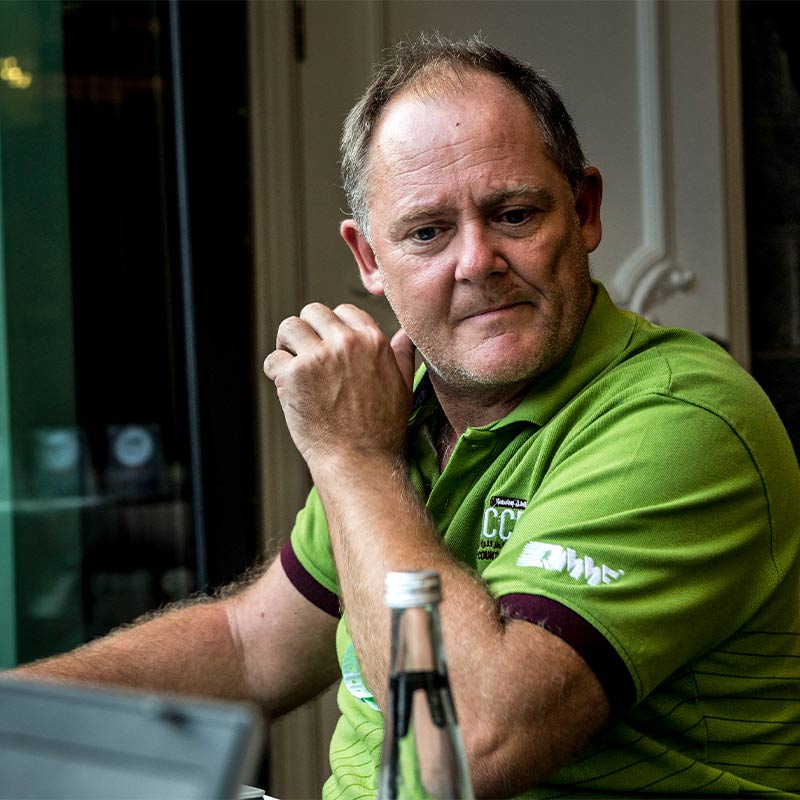 Neil Perkins sits behind desk in green t-shirt.