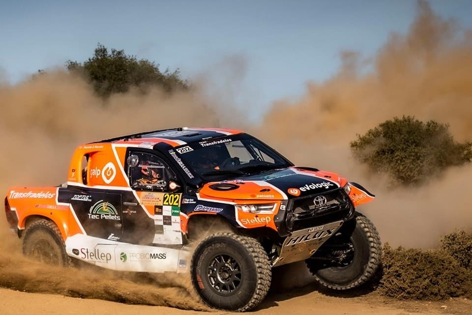 A rally car sprays up sand as it races along a dirt track.